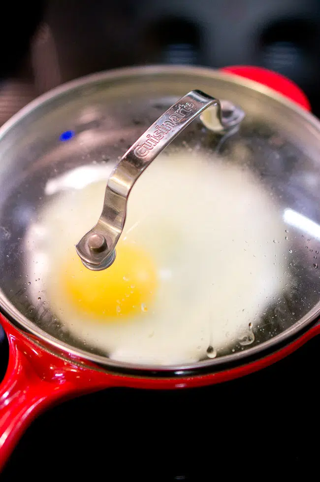 An egg gently cooking in a pan, covered with a lid, illustrating the steaming technique for a perfect fried egg.