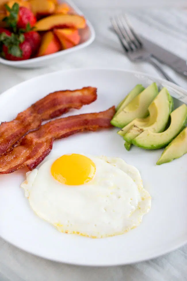 A perfectly fried egg served with crispy bacon and creamy avocado slices, ready for a delicious breakfast or brunch.