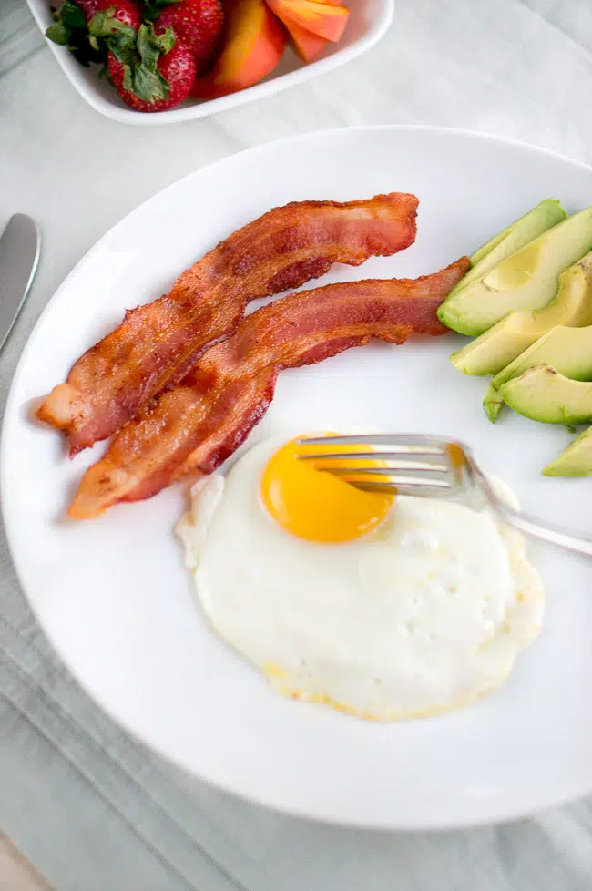 A fork piercing the runny yolk of a perfectly fried egg, highlighting its appealing texture.