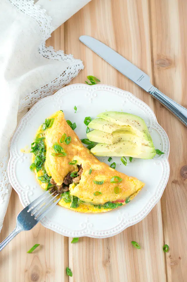 Close-up of a folded Kale and Sausage Omelet on a white plate, ready for breakfast.