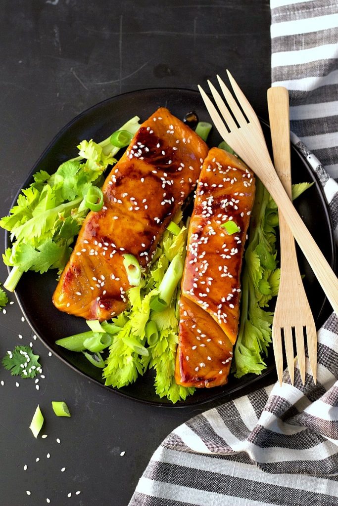 Asian teriyaki salmon on black plate with fresh greens