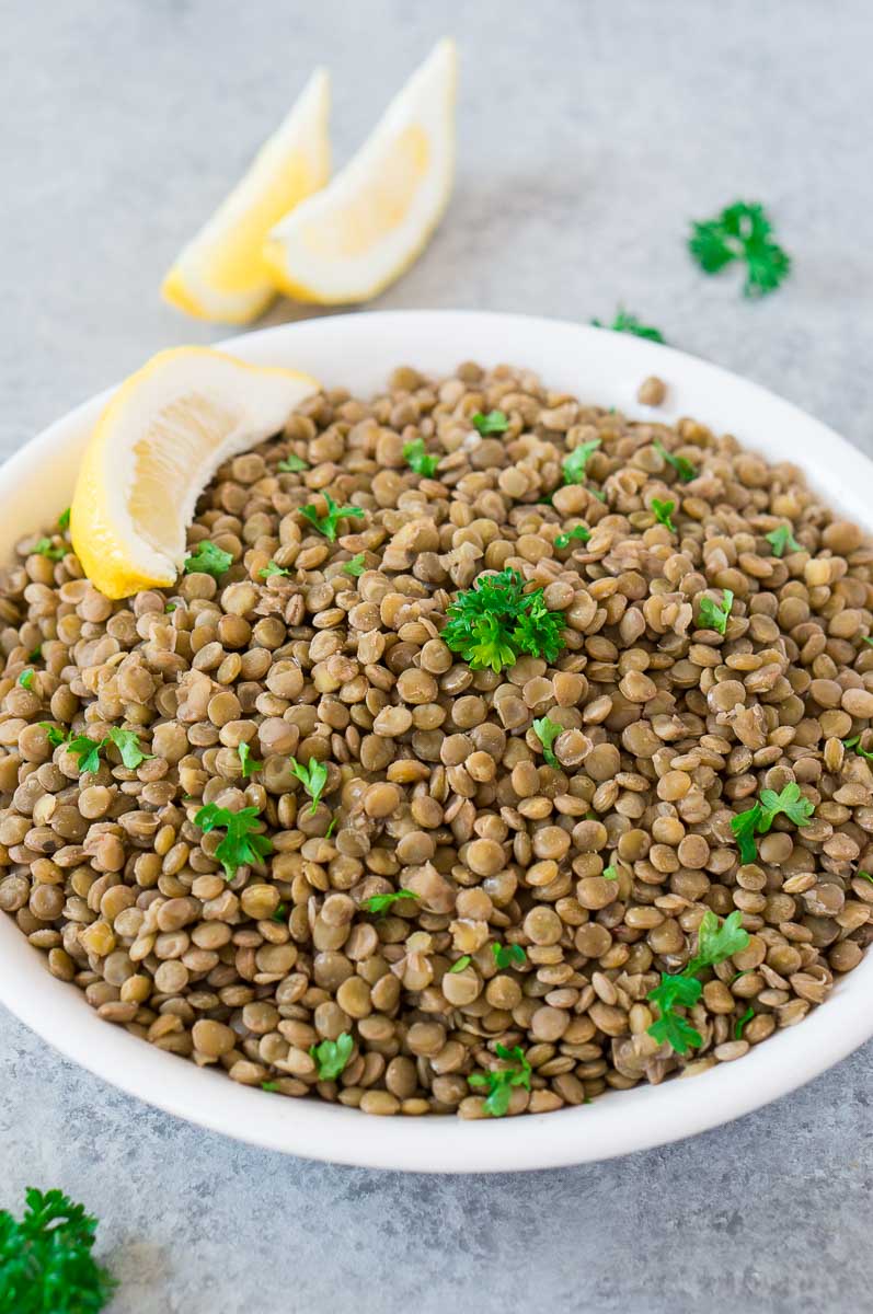 cooked lentils in a white bowl with parsley & lemons