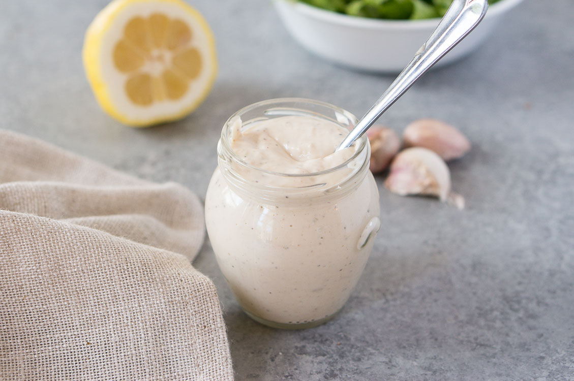 homemade caesar dressing in a glass jar with lemon and garlic in the background