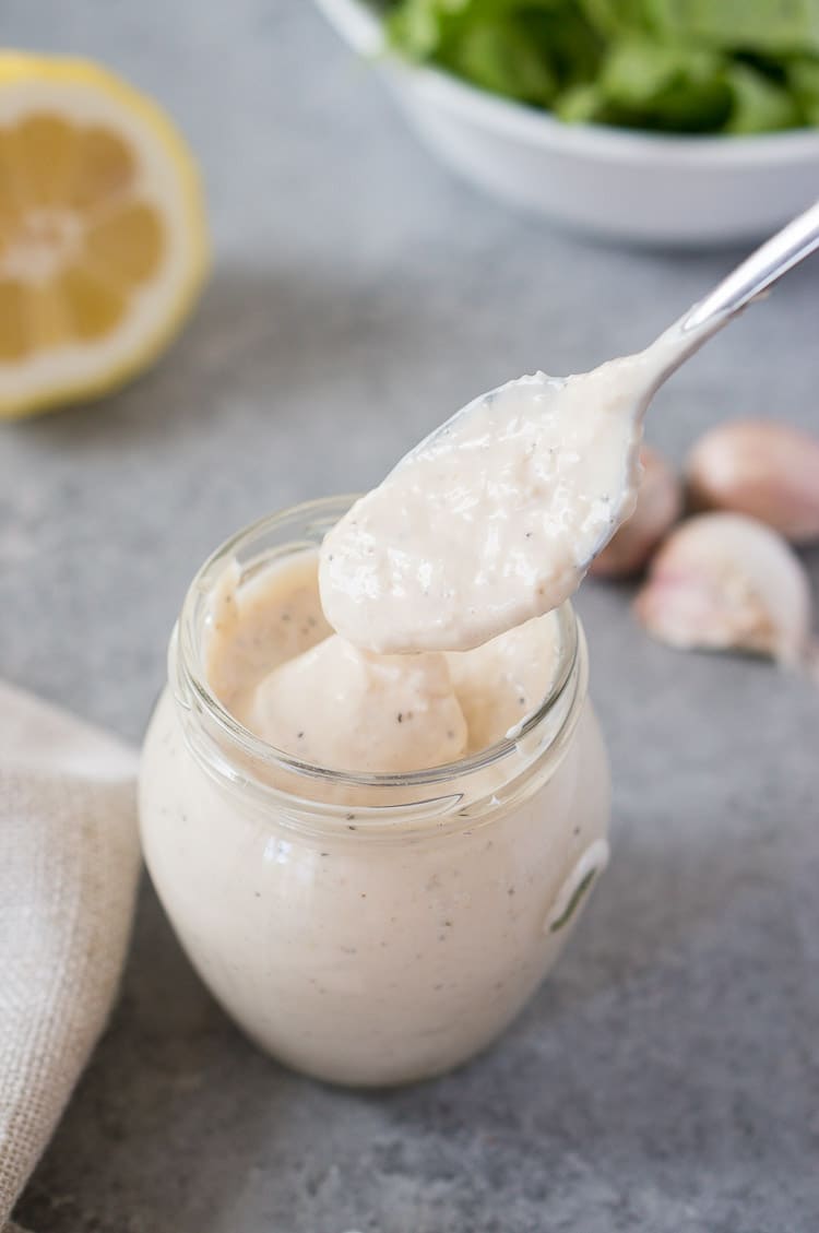 scooping caesar dressing with a spoon from glass jar