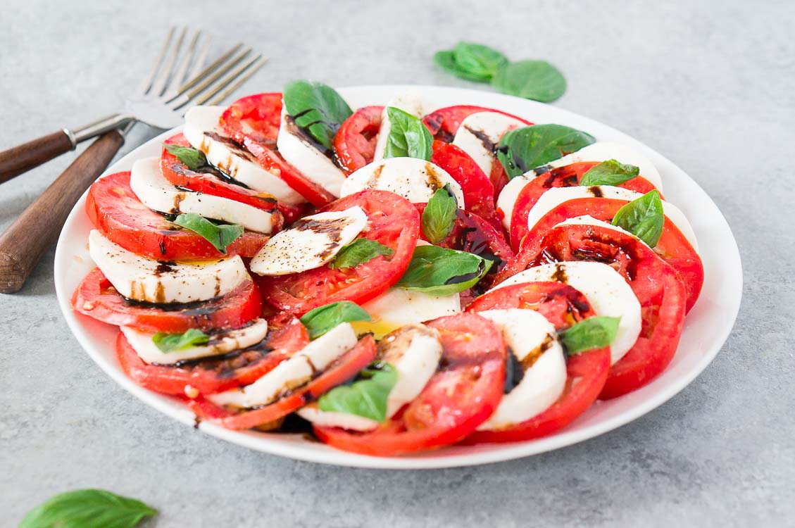 layered caprese salad on a white plate and gray board