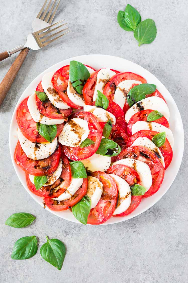 tomato mozzarella caprese salad on a plate with basil and forks in the background