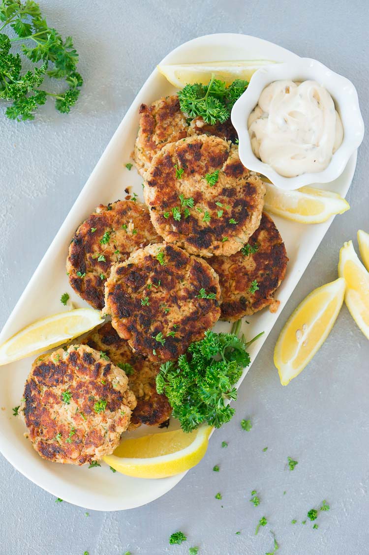 best salmon patties plated with lemon wedges and tartar sauce and parsley on a board
