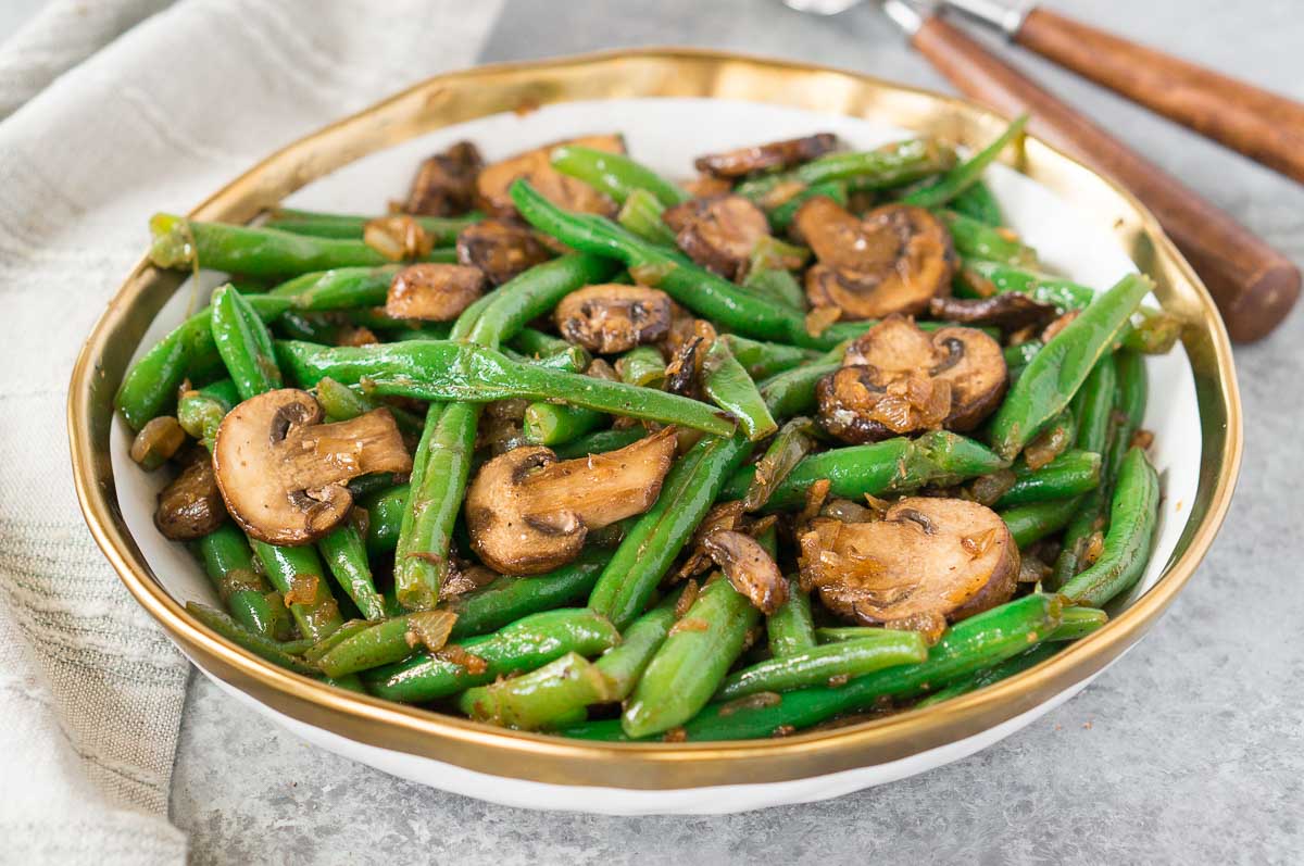 healthy green beans and mushrooms on a board with fork and napkin in background