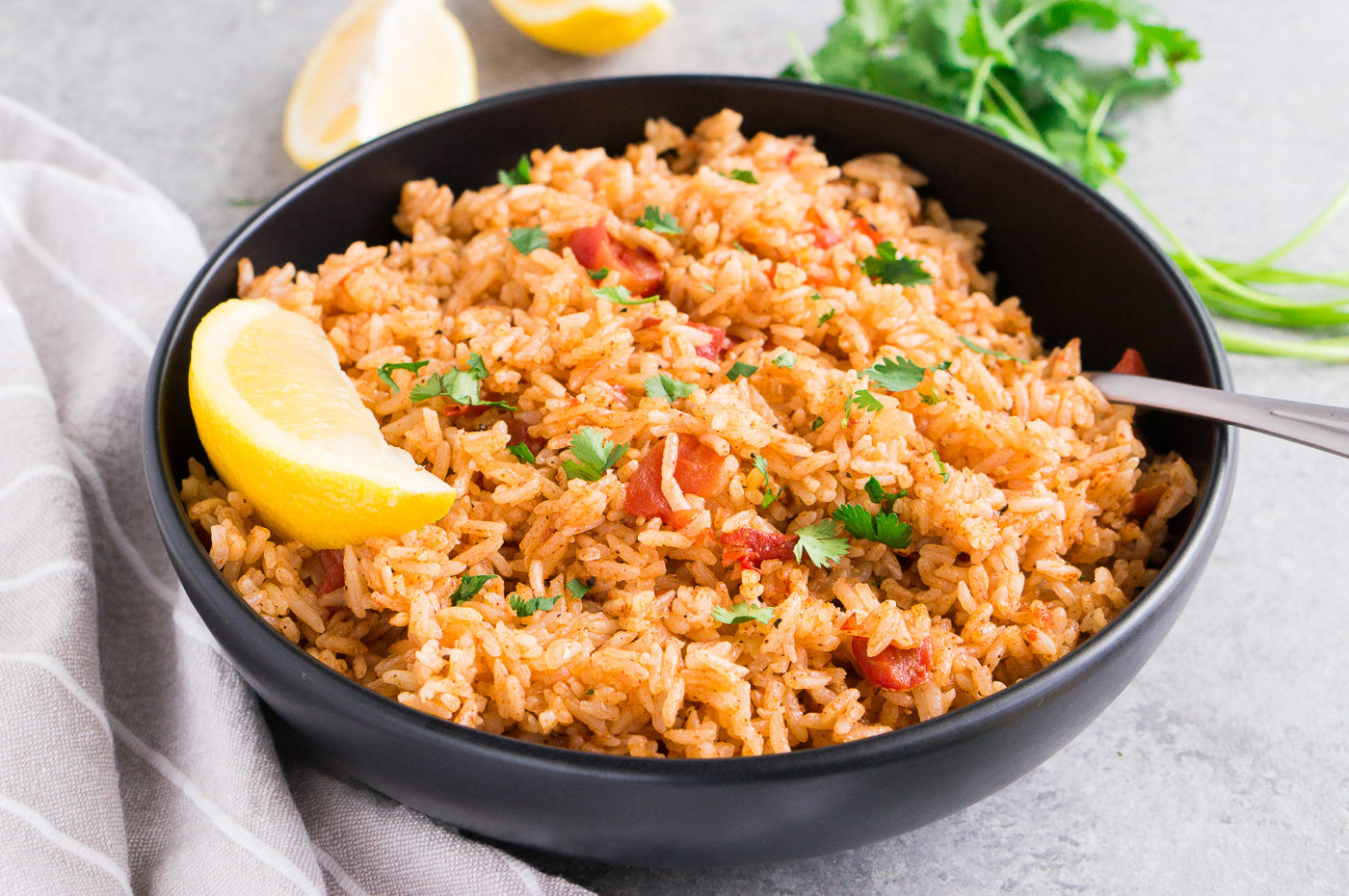 spanish rice in a black bowl with lemon wedge