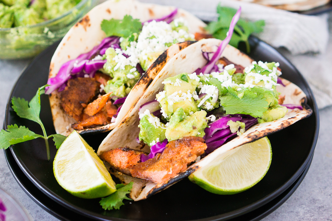 close up of salmon tacos with avocado salsa on black plates
