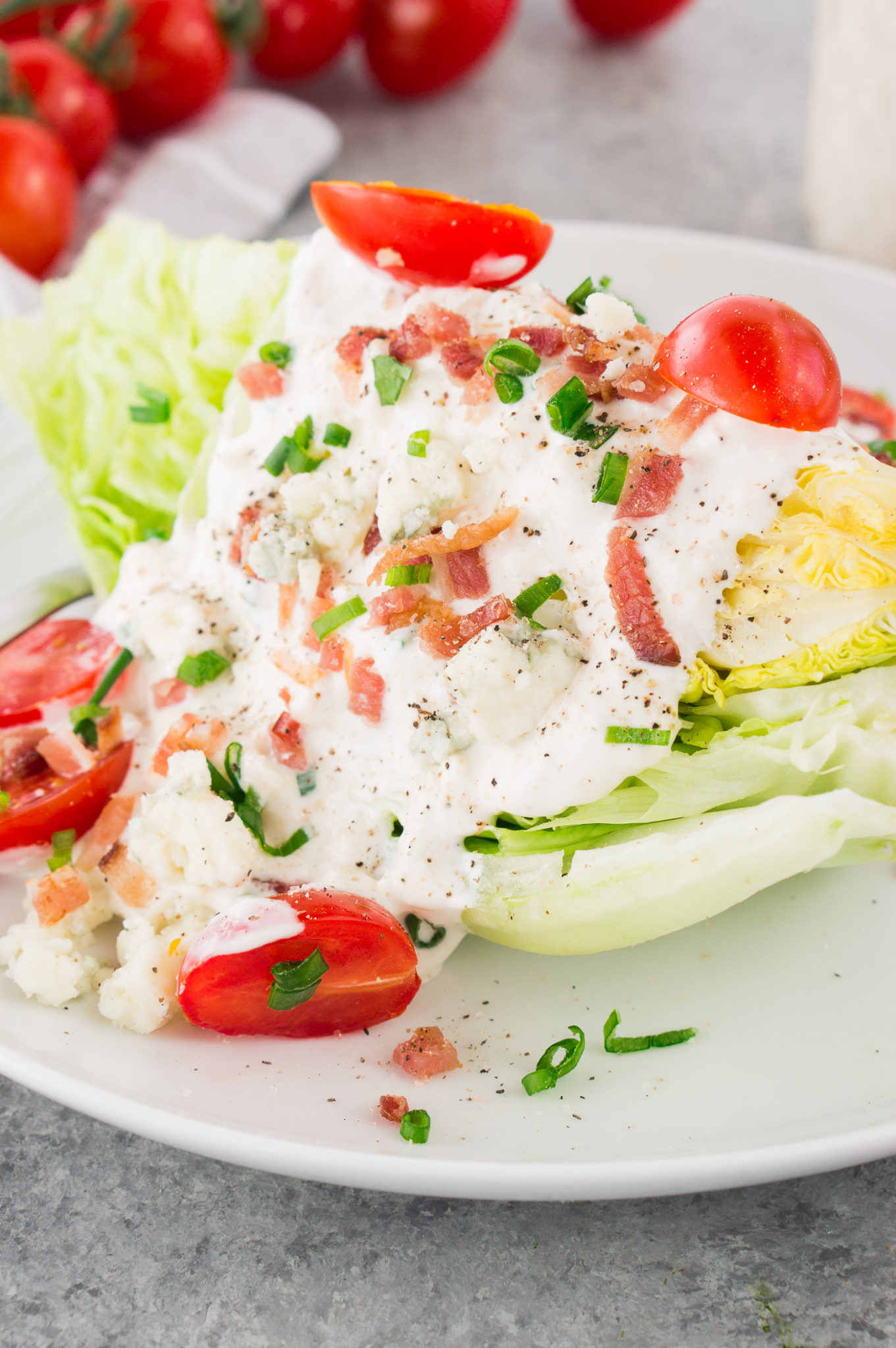 close up shot of iceberg wedge salad drizzled with blue cheese dressing tomatoes and bacon served on a plate