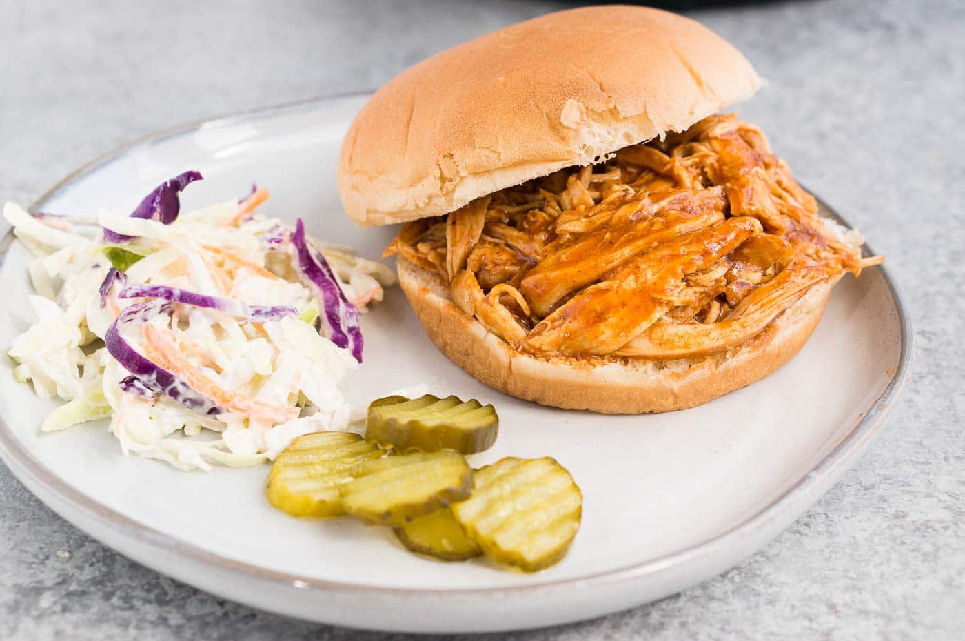 instant pot pulled chicken on a bun served with pickles and slaw