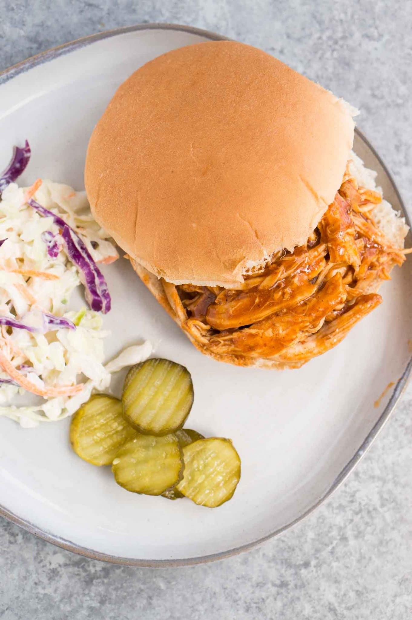 pressure cooker pulled chicken served on a bun with slaw and pickles