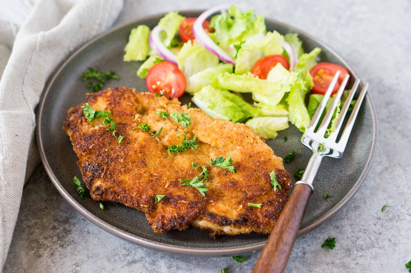 close up image of chicken milanese on a plate with a salad