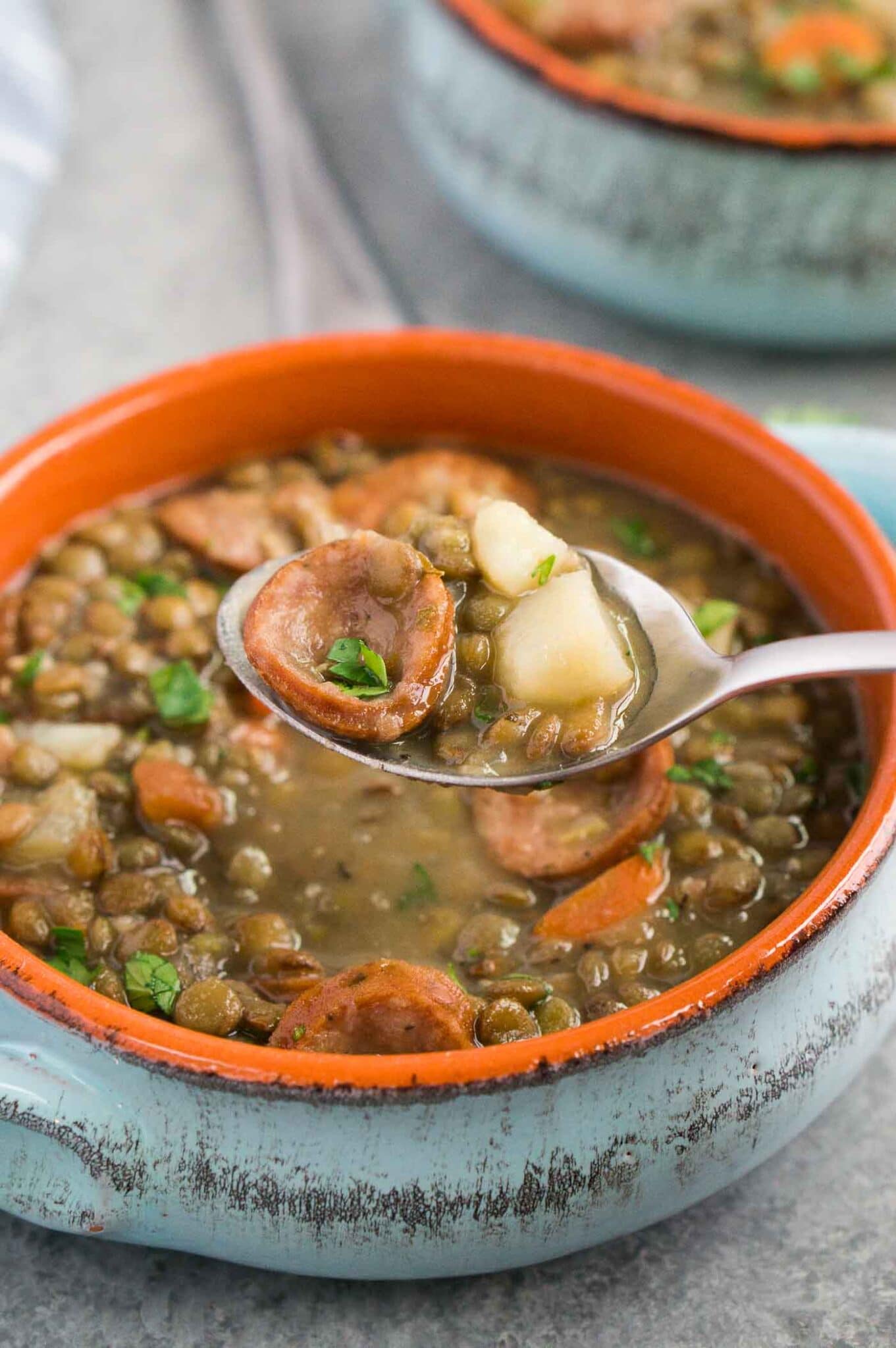 scooping lentil and sausage soup from a bowl