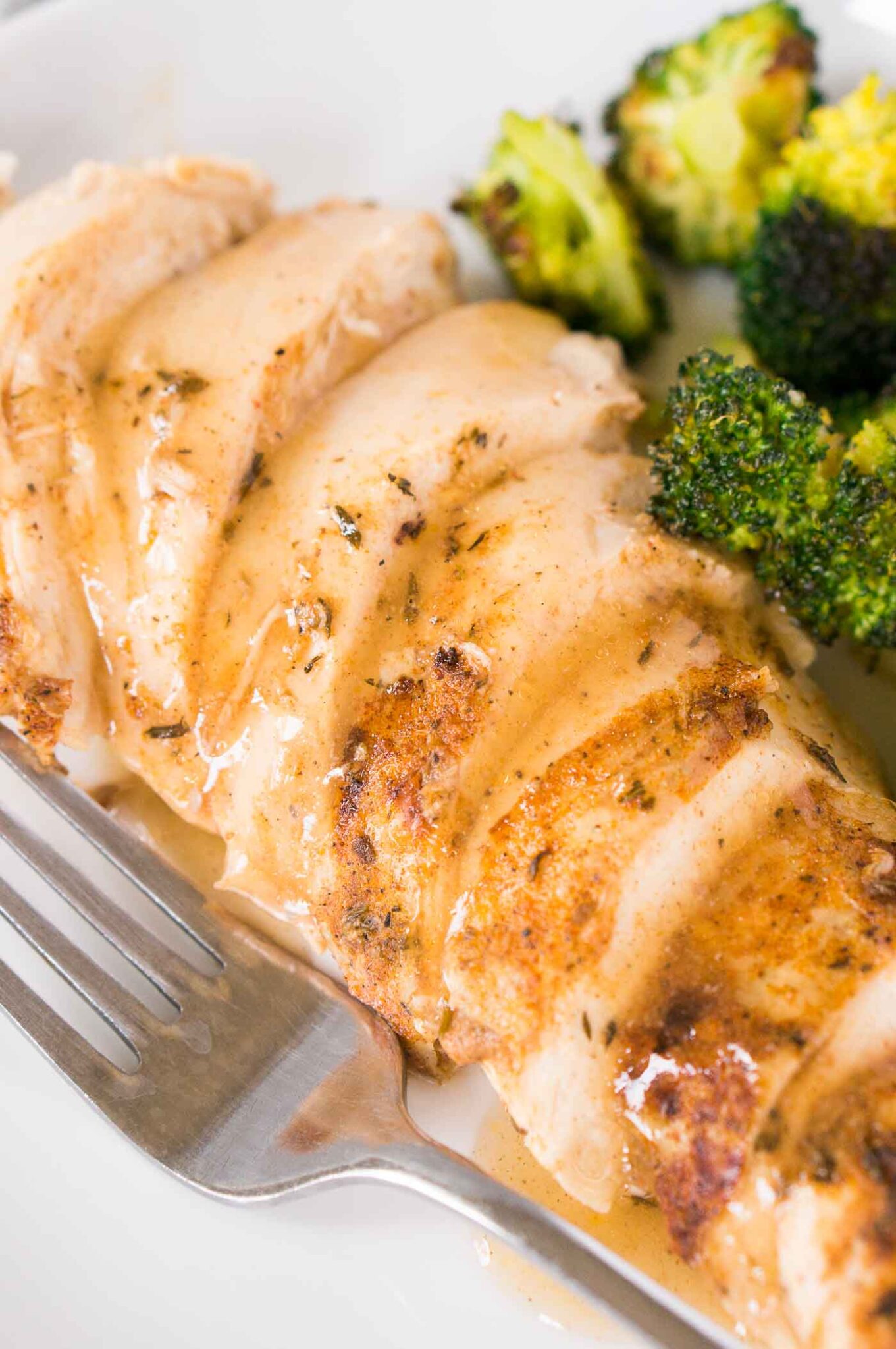 close up image of sliced chicken breast and gravy on a plate with broccoli