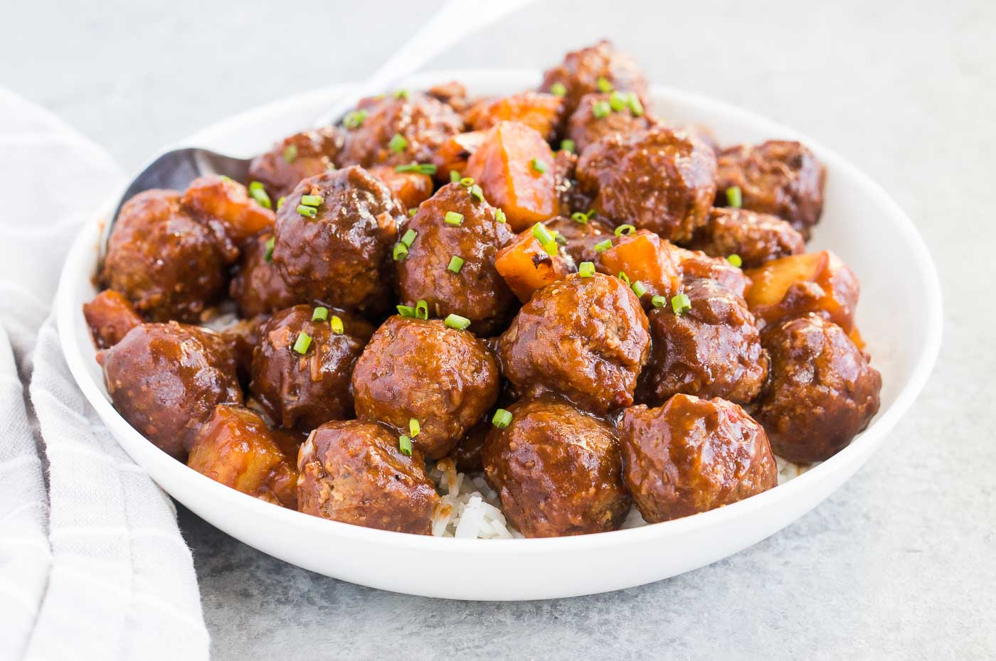 close up image of meatballs and pineapple chunks over rice in a bowl
