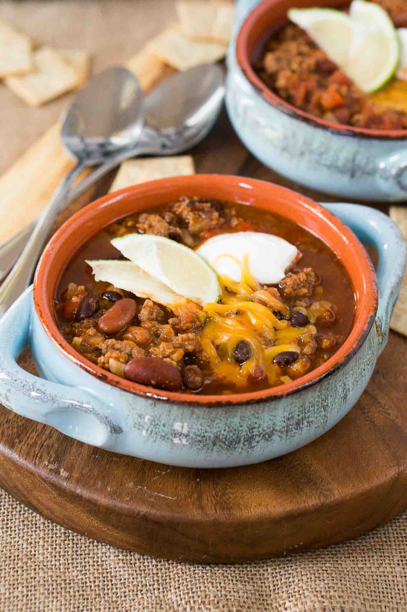 chili topped with sour cream, cheese and lime slices in a bowl