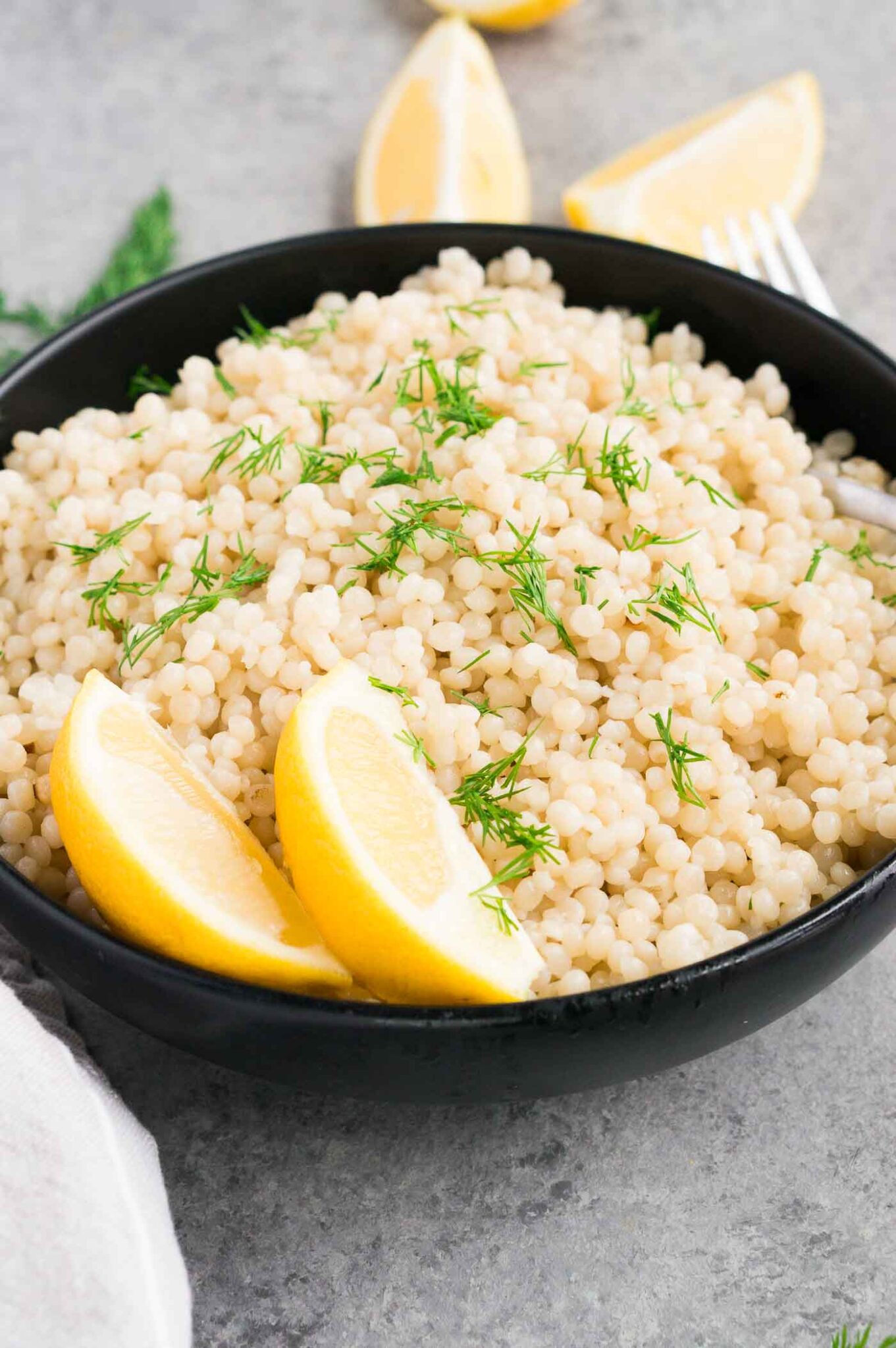 cooked pearl couscous and lemon slices in a black bowl