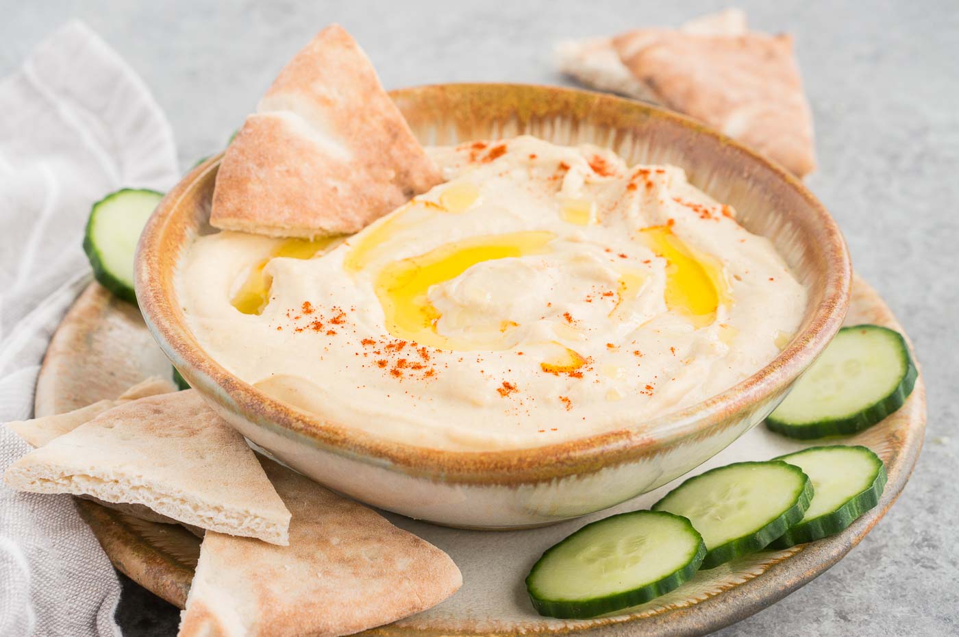 authentic hummus made at home served in a bowl with cucumber and pitas