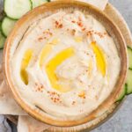 smooth and creamy hummus in a bowl with cucumbers and pita