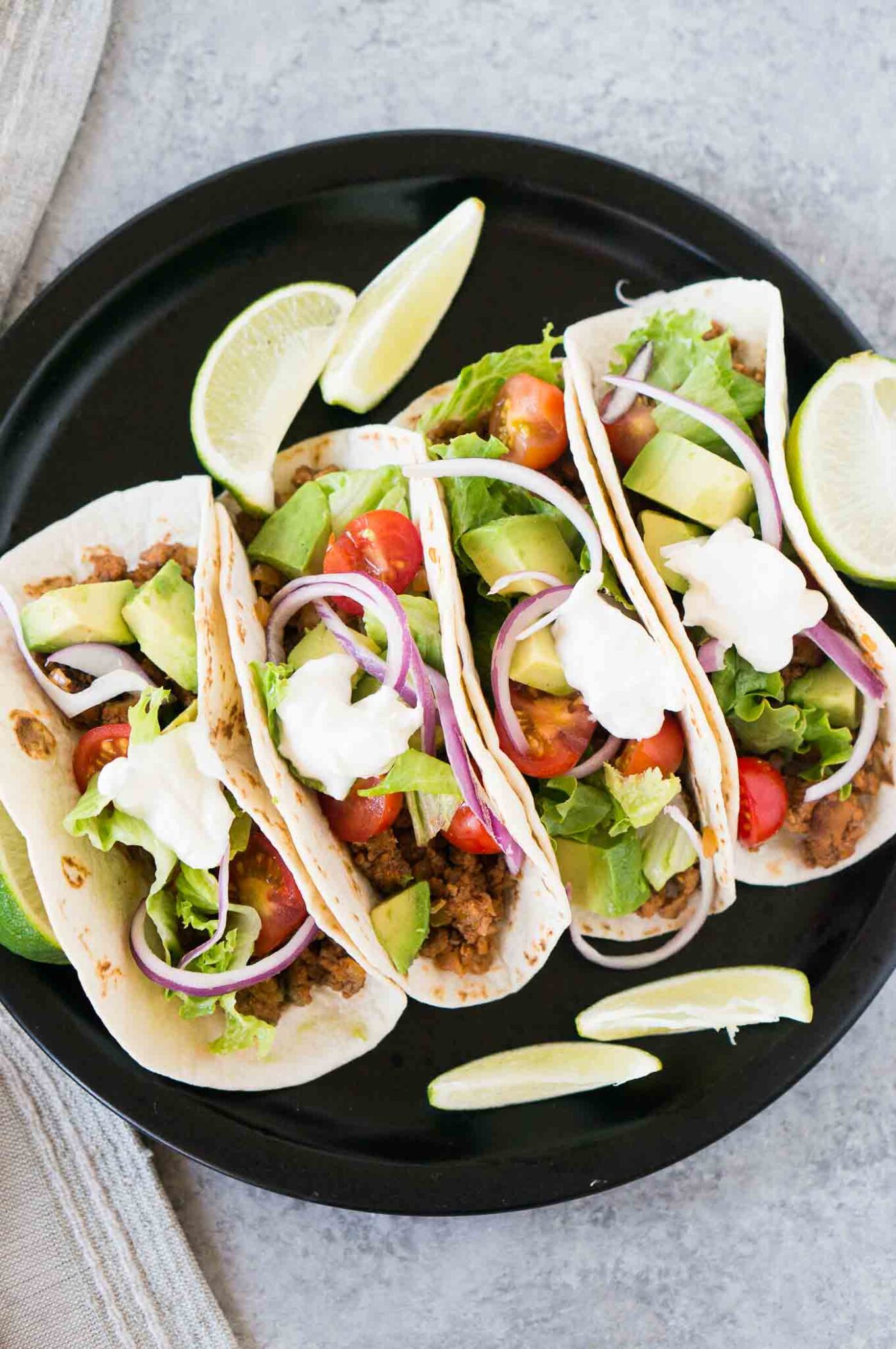 four tacos on a plate with lime wedges