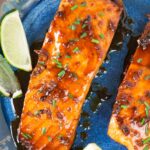 close up image of honey glazed salmon on a blue plate with lime wedges