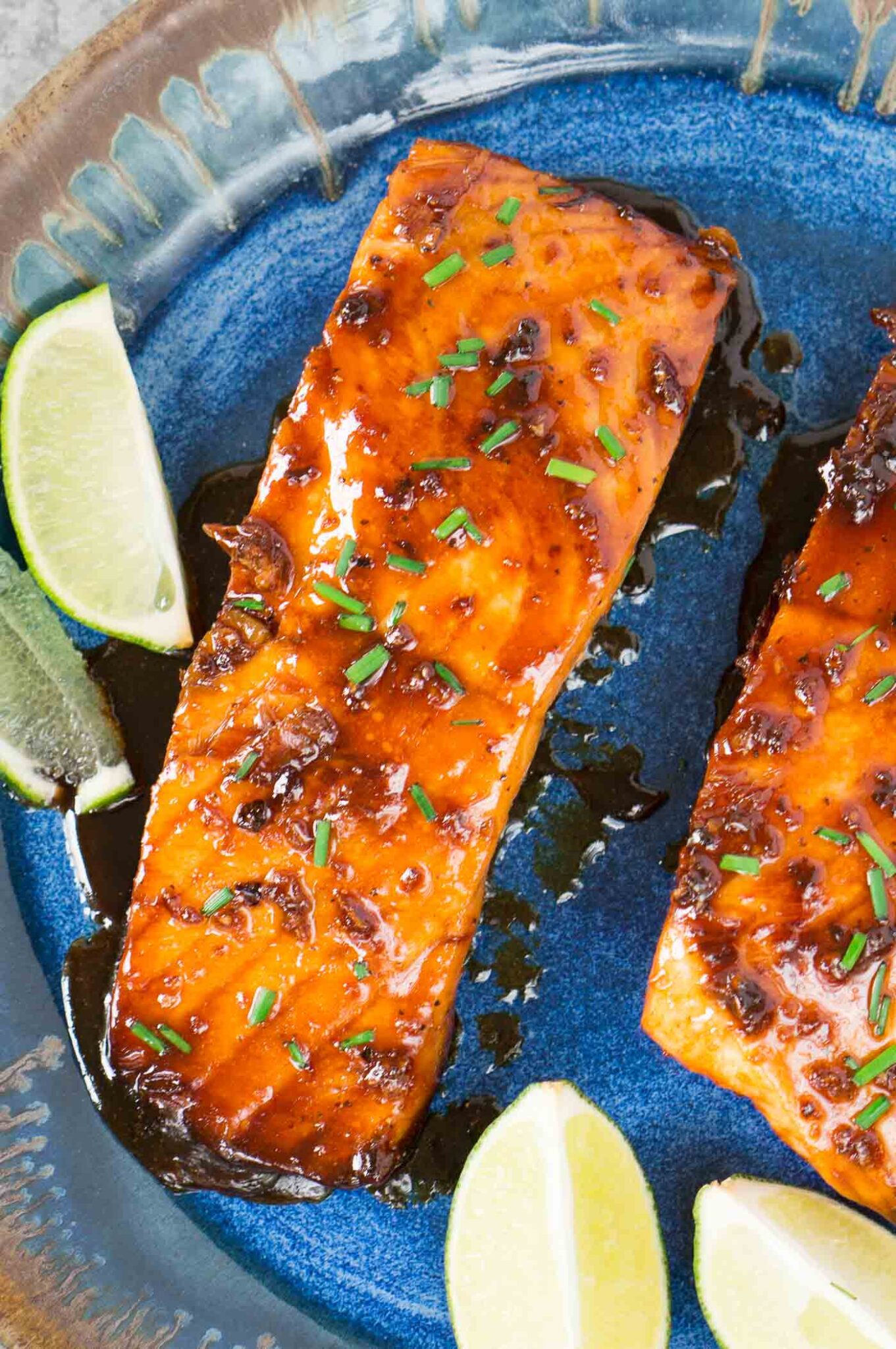 close up image of honey glazed salmon on a blue plate with lime wedges