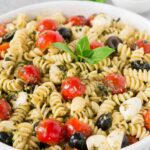 close up image of pesto pasta salad with tomatoes and olives and mozzarella balls