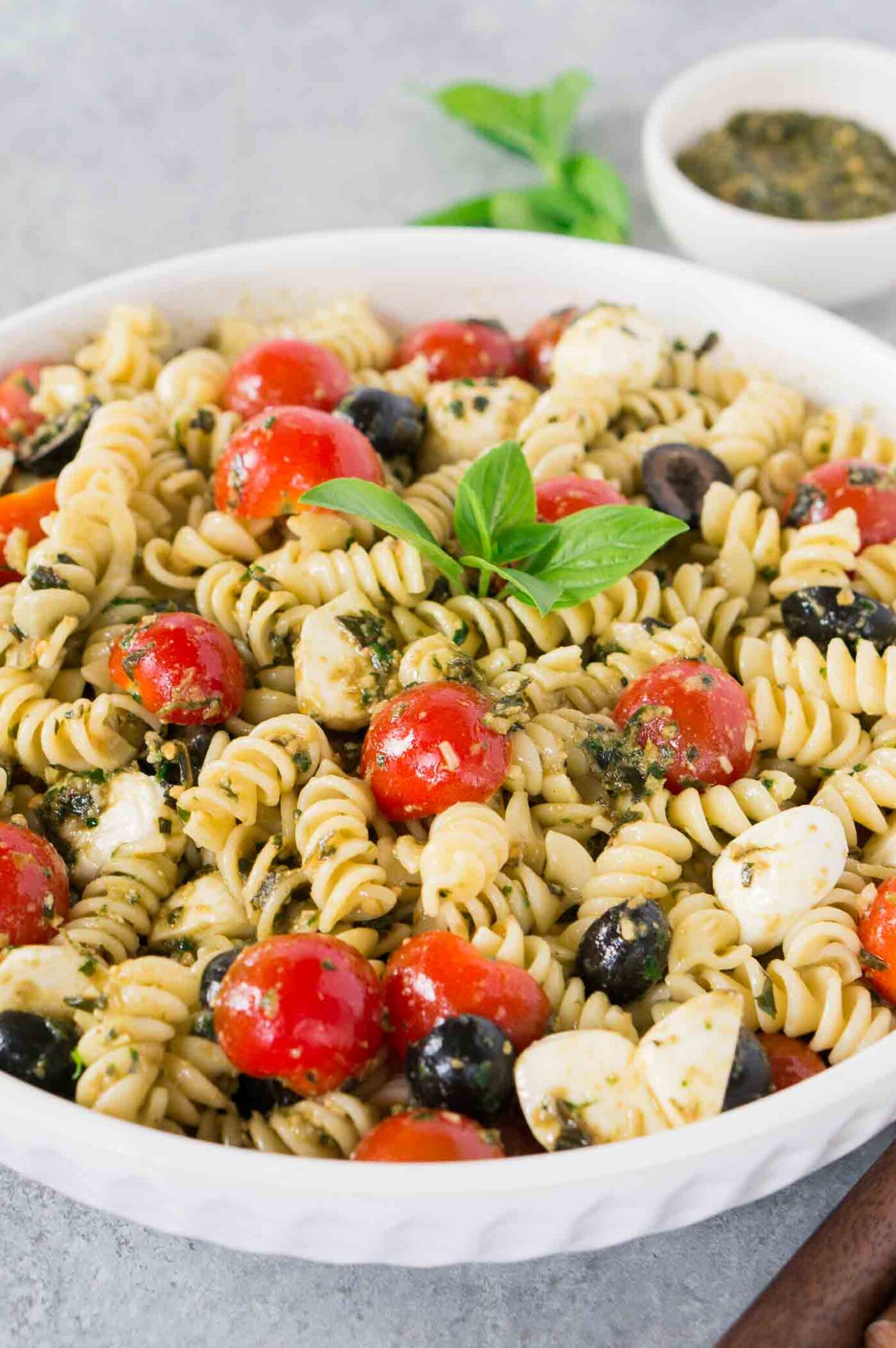 close up image of pesto pasta salad with tomatoes and olives and mozzarella balls