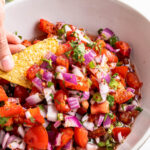 close up image of fresh pico de gallo in a white bowl with corn chip
