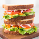 hummus and veggie sandwich on a wooden cutting board