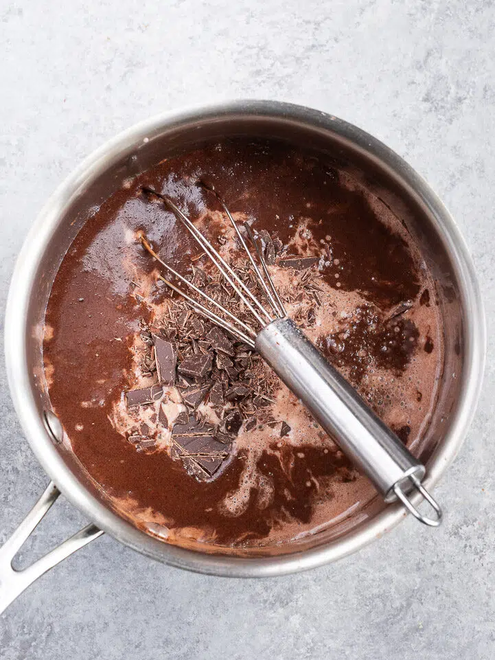Continuously whisking the hot chocolate mixture in a saucepan as it heats