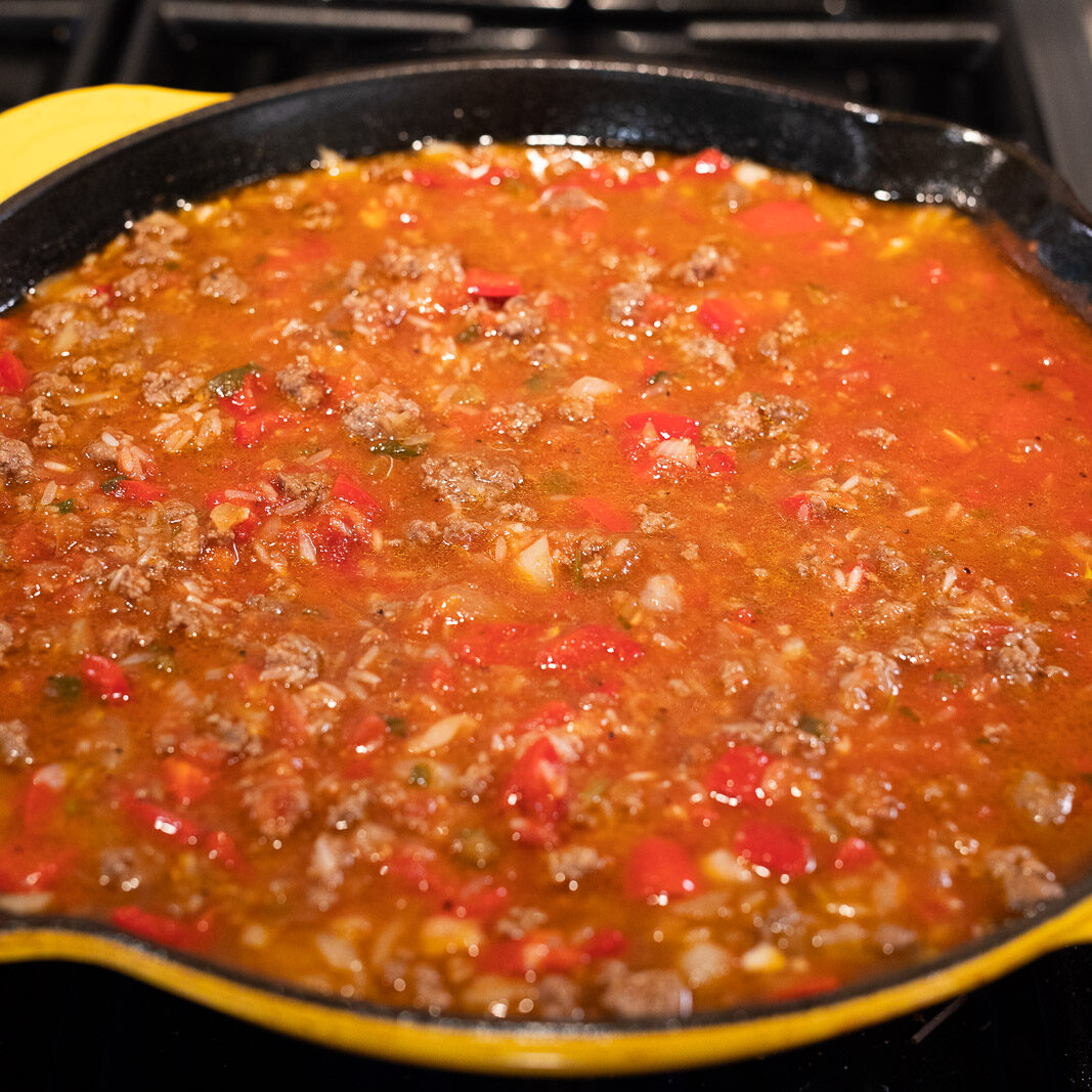 cooking rice, tomato sauce with beef and vegetables in a skillet