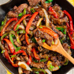 pepper steak in a skillet with a wooden spoon