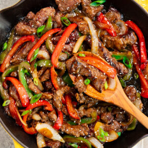 pepper steak in a skillet with a wooden spoon