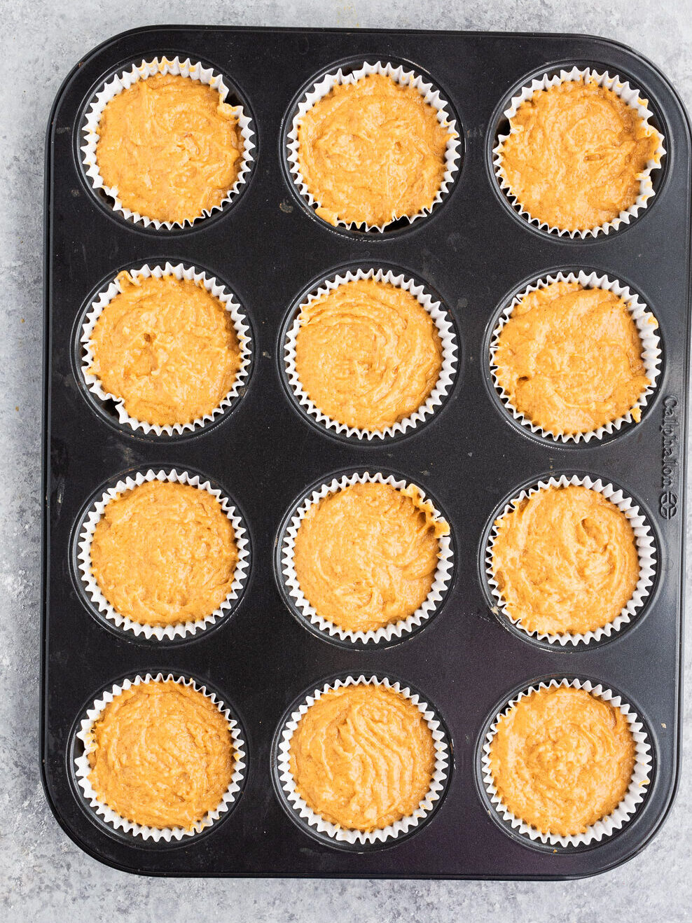 filling muffin tin with pumpkin batter