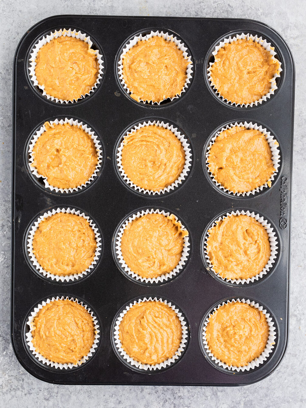 filling muffin tin with pumpkin batter
