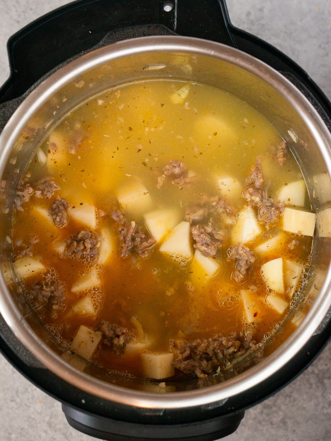 adding potatoes, stock and seasonings to zuppa toscana