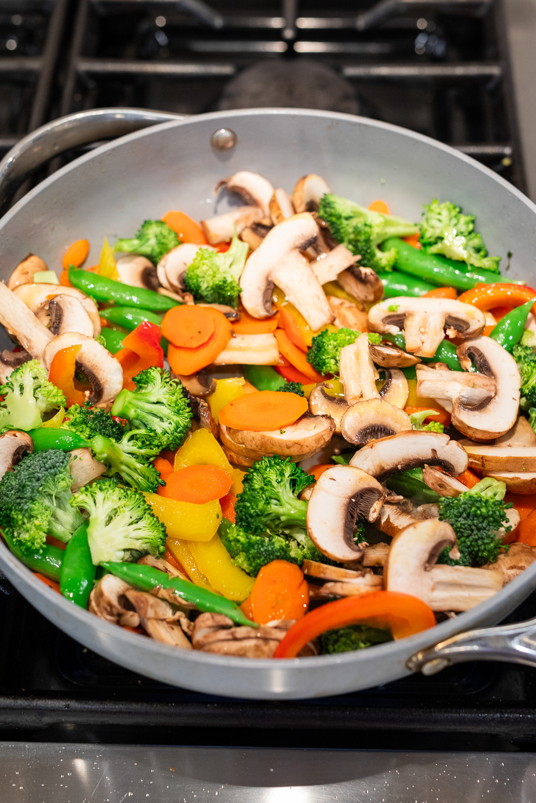 Fresh vegetables cooking in a skillet for easy vegetable stir fry, including broccoli, mushrooms, bell peppers, carrots, and snap peas