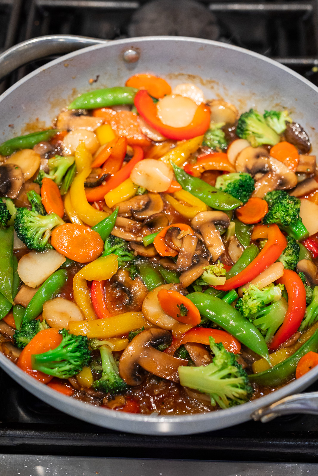 simple vegetable stir fry simmering in a skillet with glossy stir fry sauce coating broccoli, mushrooms, bell peppers, carrots, and snap peas