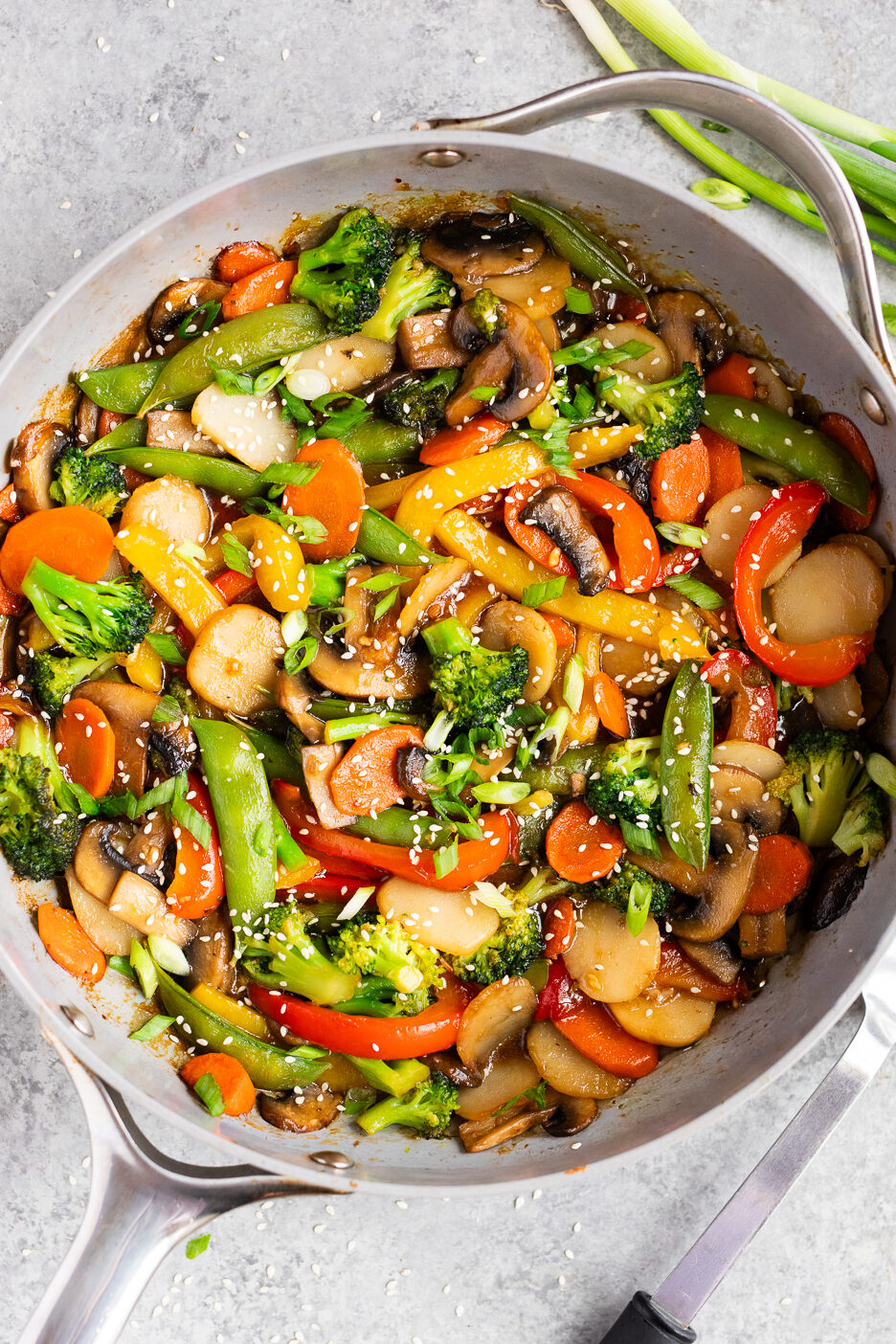 Finished weeknight vegetable stir fry garnished with green onions and sesame seeds, served straight from the skillet