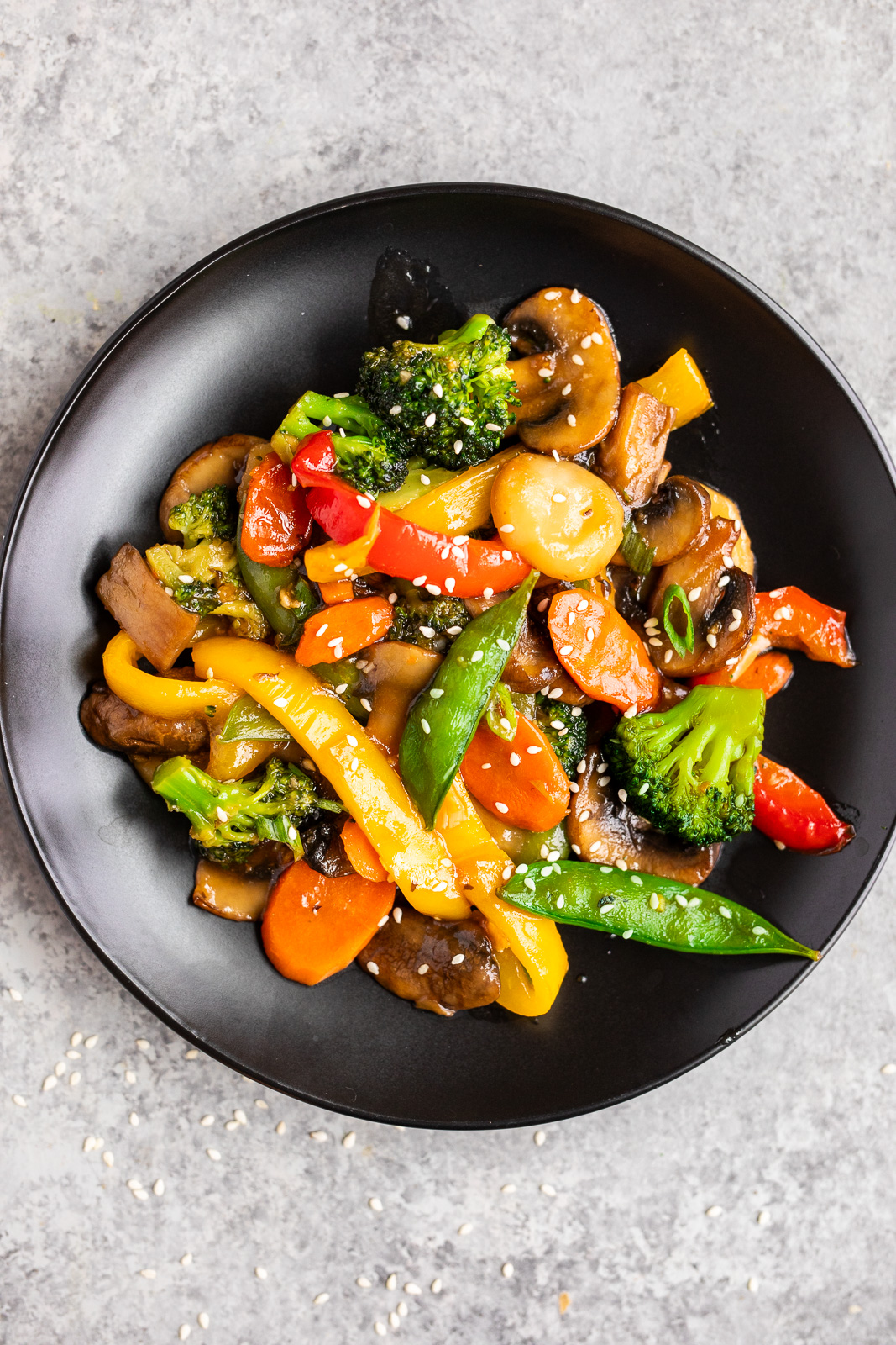 Easy vegetable stir fry with broccoli, bell peppers, mushrooms, carrots, sugar snap peas, and sesame seeds served on a black plate