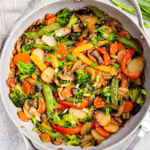Healthy vegetable stir fry cooked in a skillet with broccoli, bell peppers, mushrooms, carrots, snap peas, and a glossy homemade stir fry sauce
