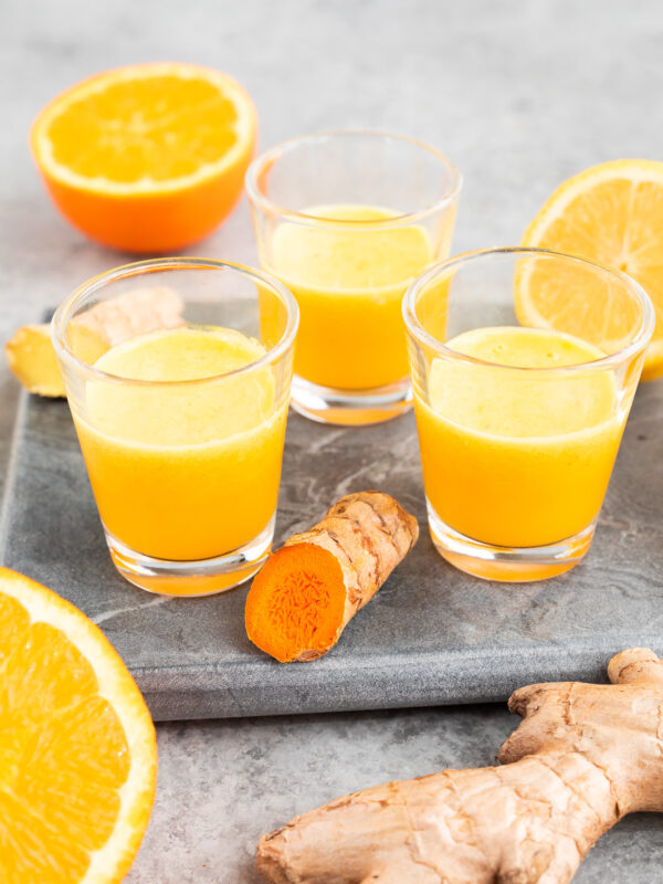 Fresh ginger turmeric shots served in small glasses with citrus