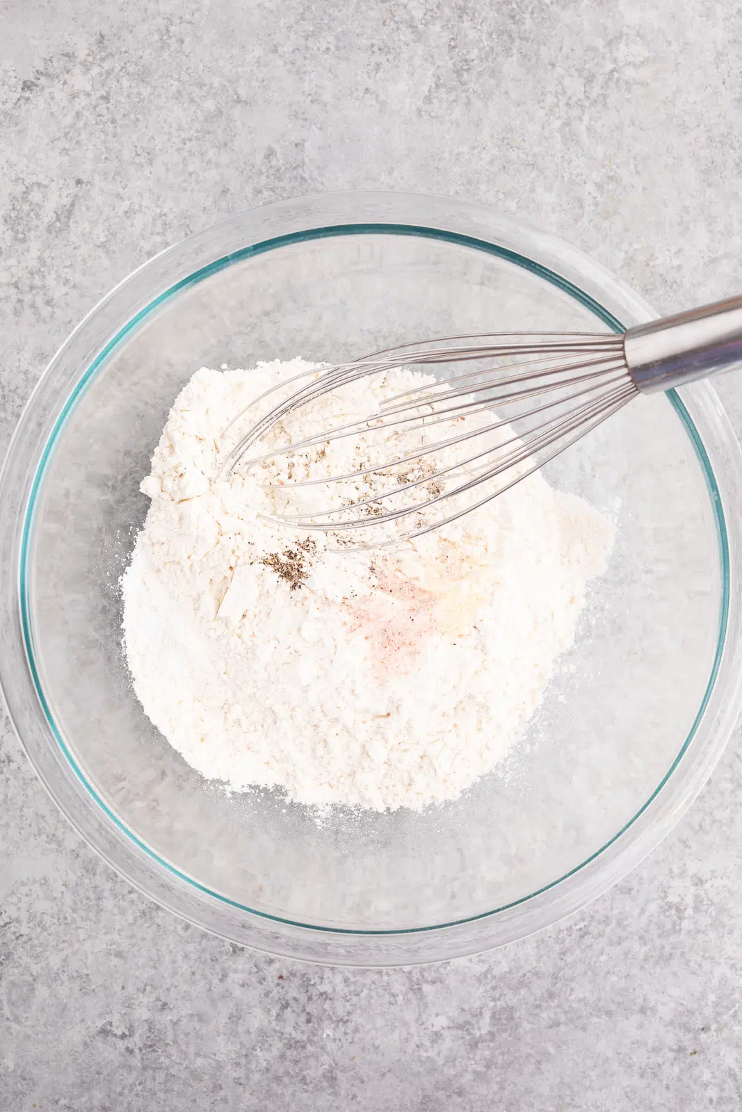 Whisking together flour, baking powder, salt, black pepper, garlic powder, and dried thyme in a large bowl for savory breakfast biscuits