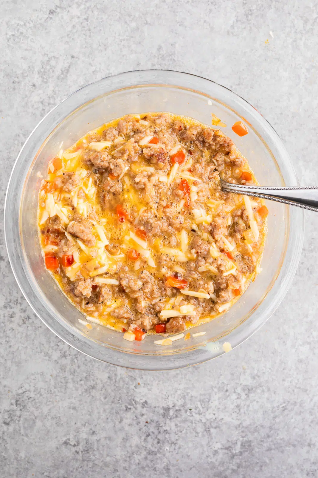 Stirring together beaten eggs, shredded cheddar cheese, and cooled sausage mixture in a bowl for breakfast biscuits