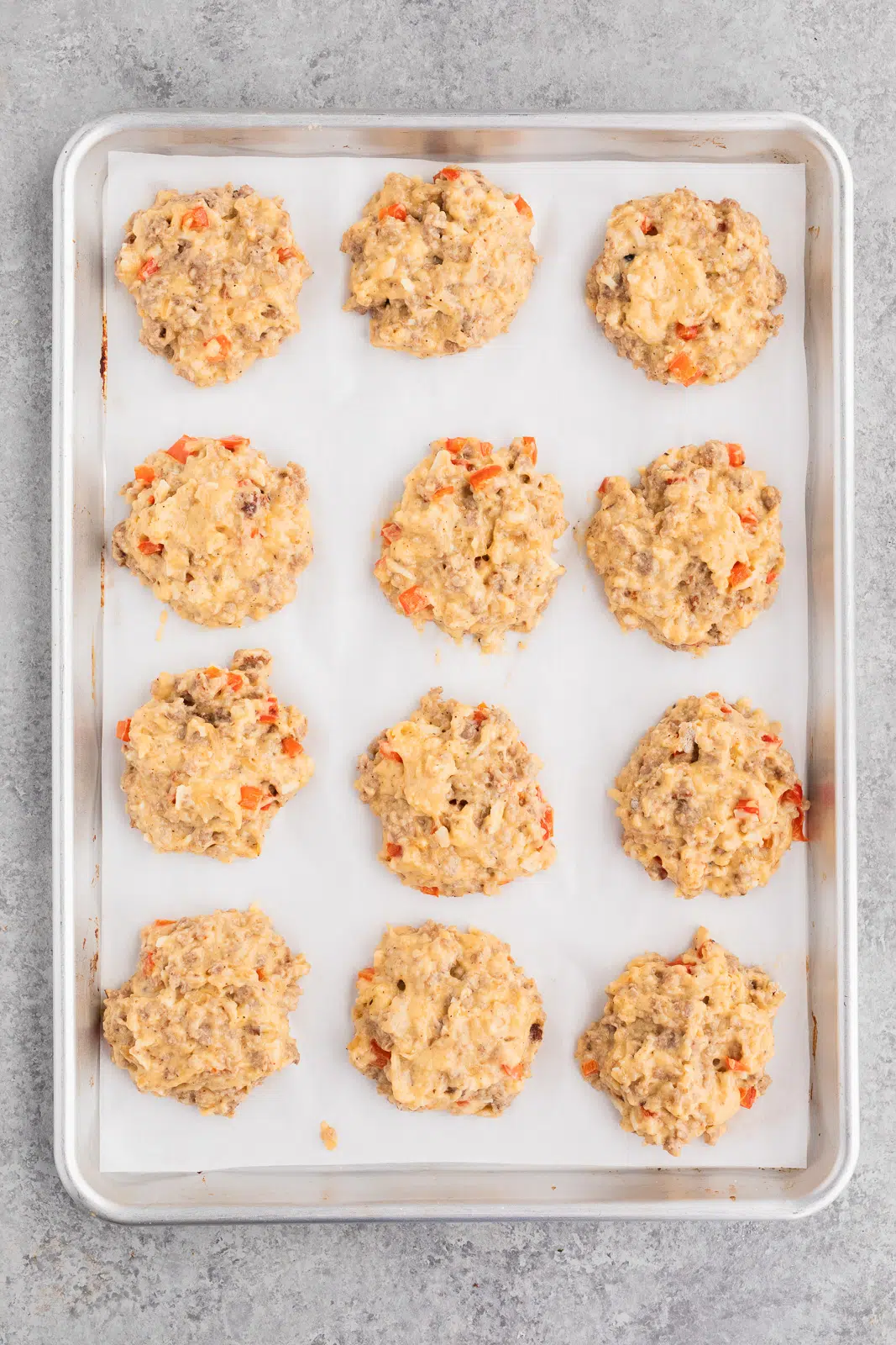 Scooping portions of thick sausage egg biscuit dough onto a parchment-lined baking sheet before baking