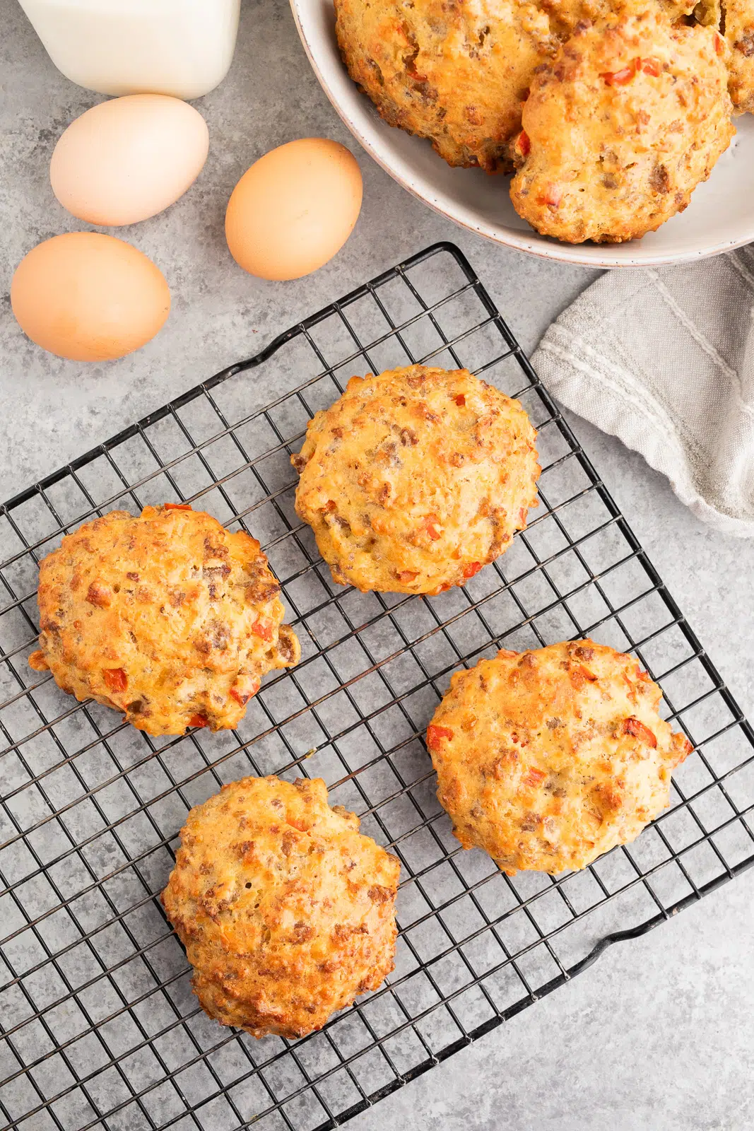 Homemade sausage breakfast biscuits with eggs and cheddar cheese cooling on a wire rack after baking