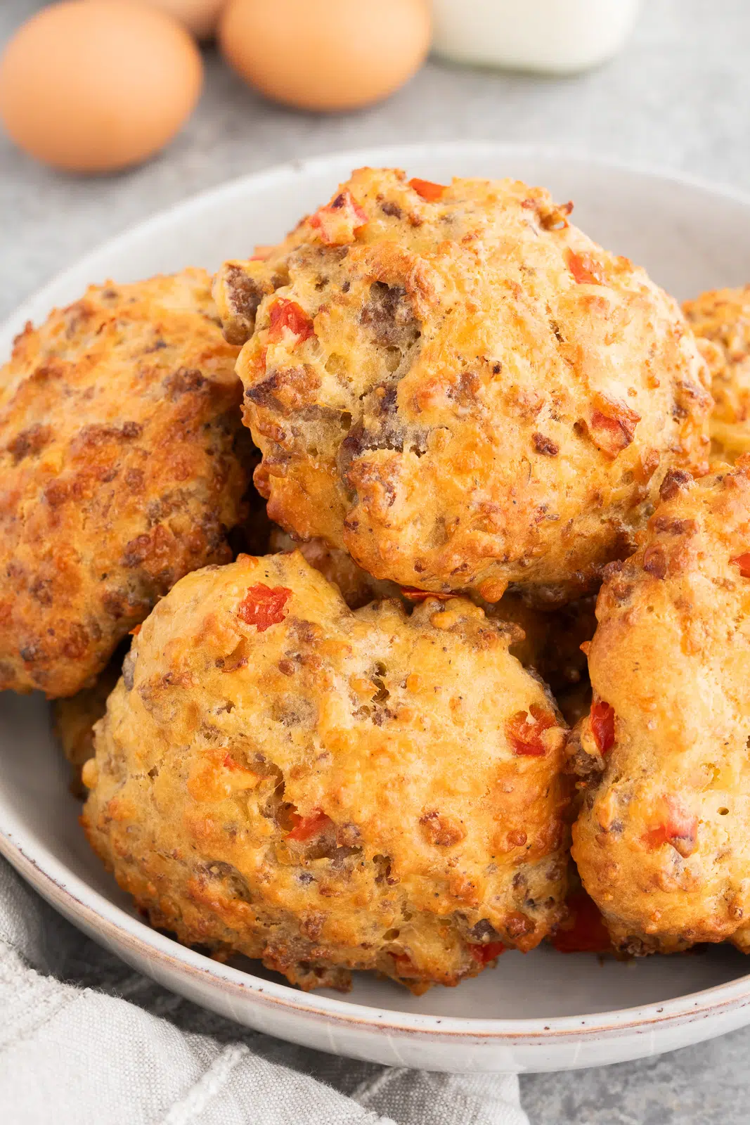 Close-up of a bowl filled with golden-brown sausage egg breakfast biscuits, showing melted cheddar cheese and savory ingredients
